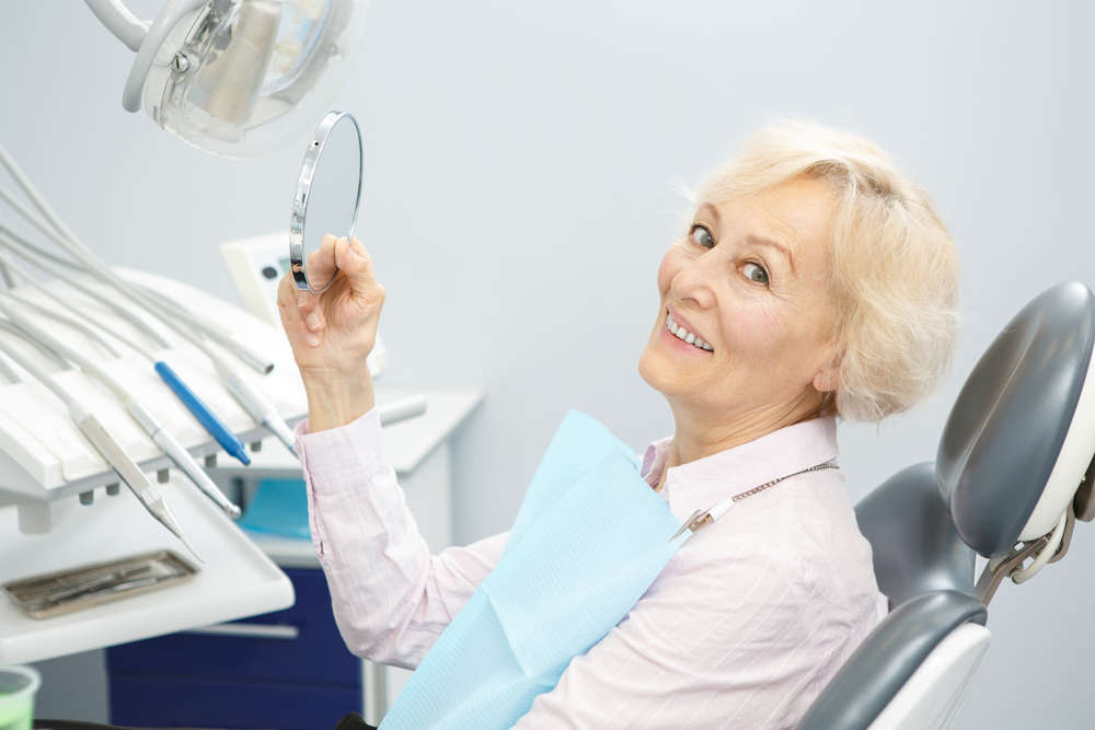 Senior,Female,Patient,Smiling,To,The,Camera,Holding,A,Mirror