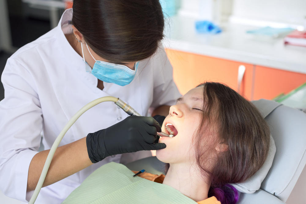 Woman,Dentist,Treating,Teeth,To,A,Patient,Sitting,In,Dental